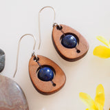 An earring of egg shaped wood frames holding round lapis lazuli beads