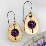 An earring of egg shaped maple wood frames holding round amethyst beads