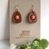 An earring of egg shaped cherry wood frames holding round coral coloredbeads