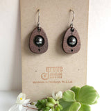 An earring of egg shaped walnut wood frames holding round black pearl beads