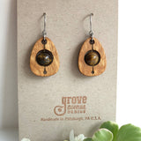 An earring of egg shaped curly maple wood frames holding round tigereye beads